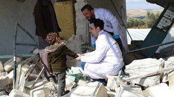 Two male doctors talk to a little boy holding his hand over rubble